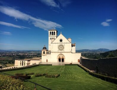 Umbria Assisi church facade - green garden - blue sunny sky- Destinations by Timeless Tuscany tour operator