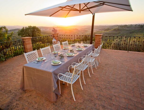 Italian dinner at Villa Bellavista on terrace at sunset; table with grey table cloth; white chairs and umbrella; Chianti hills view - villa rentals by Timeless Tuscany tour operator