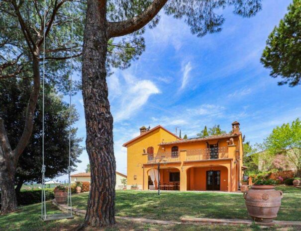 Villa Bellavista garden with pine and olive trees in a sunny day with blue sky; main villa with front porch in the Chianti region